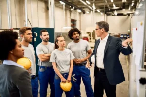 Grupo de trabajadores de industria con cascos de seguridad atentos a la explicación de su responsable sobre formaciones obligatorias de PRL